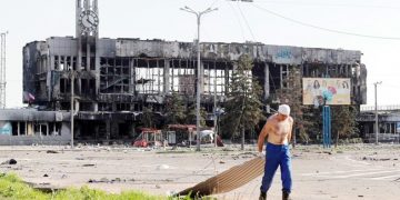 A man drags metal board near a railway station building destroyed in the southern port city of Mariupol, Ukraine
